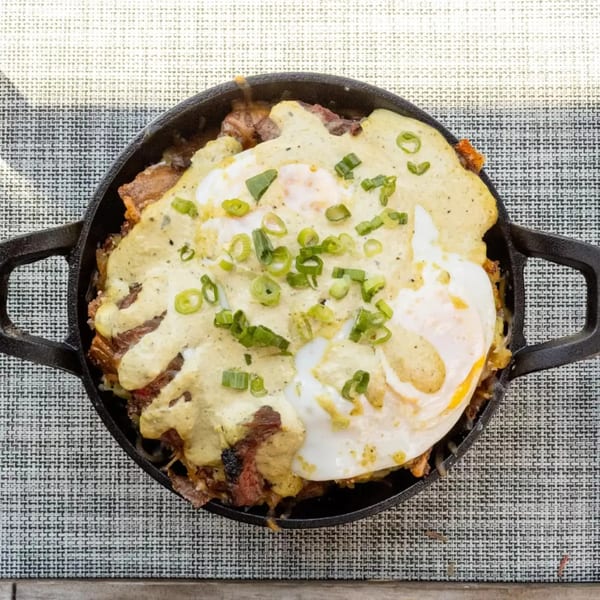 Breakfast skillet with fried eggs, green onions, and a creamy sauce over potatoes and meat.