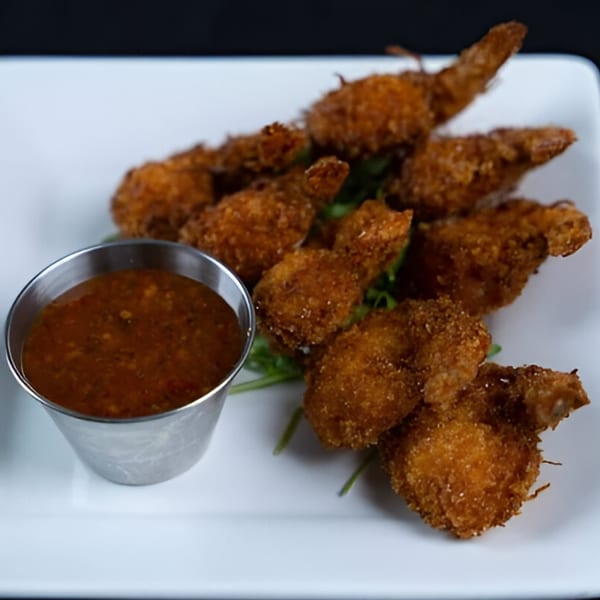 Crispy fried shrimp with a side of dipping sauce on a white rectangular plate.