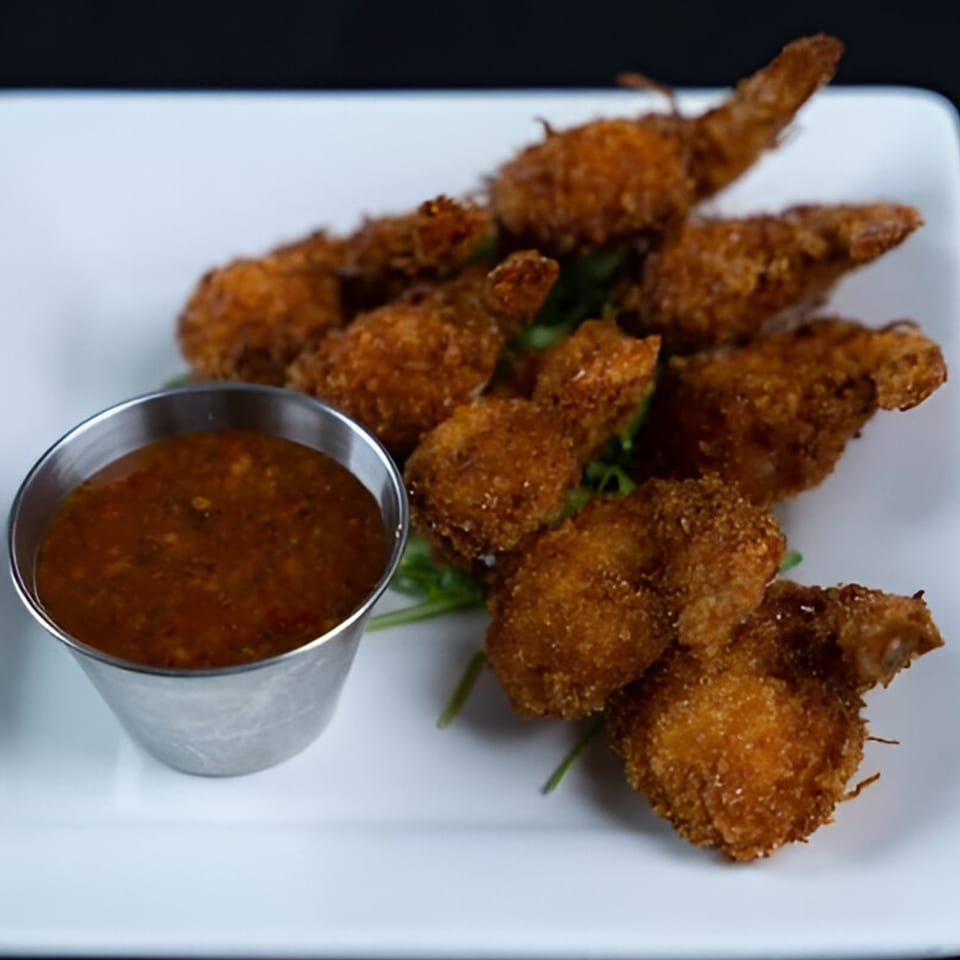 Crispy fried shrimp with a side of dipping sauce on a white rectangular plate.