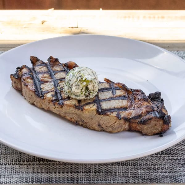 Grilled steak with grill marks and a dollop of herb butter on a white plate.