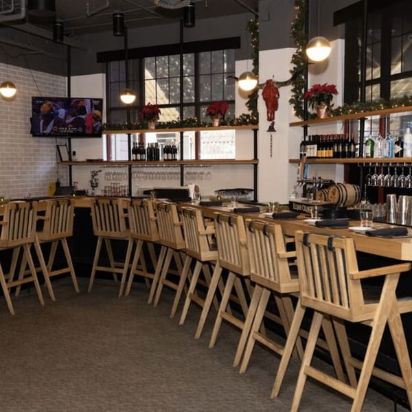 A long wooden bar with high-backed wooden chairs, bottles of alcohol, and a TV showing sports.