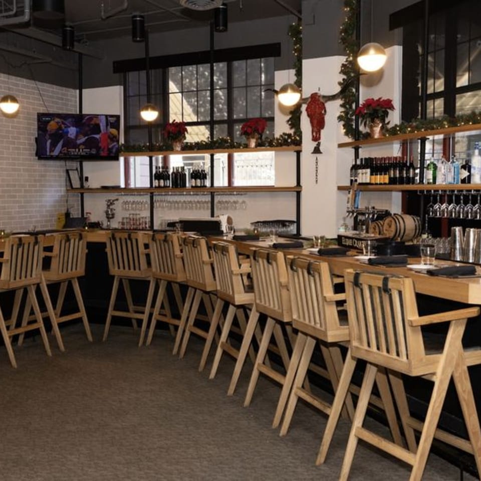 A long wooden bar with high-backed wooden chairs, bottles of alcohol, and a TV showing sports.