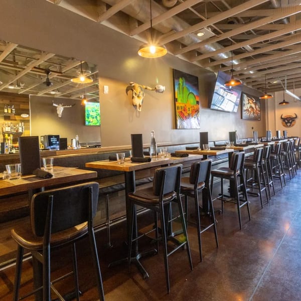 Restaurant interior with high-top tables, bar stools, and bull skull decor under exposed ceiling beams.