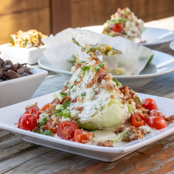 Wedge salad with blue cheese dressing, bacon, and cherry tomatoes on a white plate.