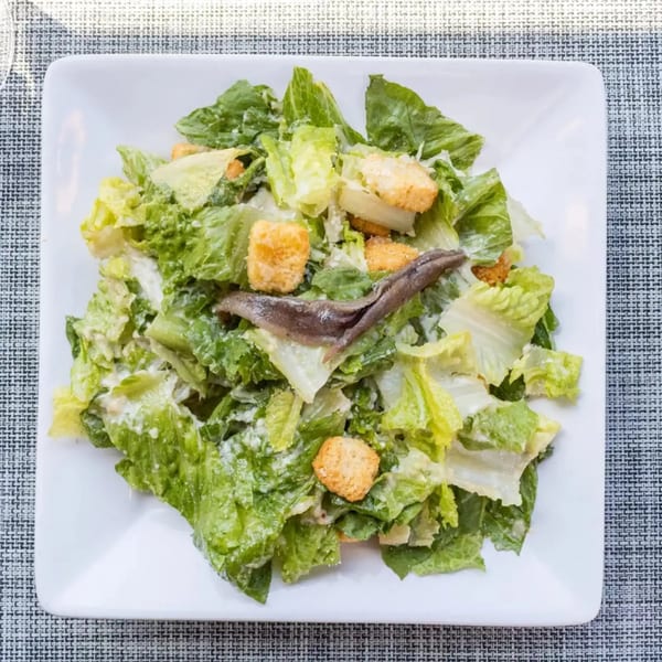 Caesar salad with romaine lettuce, croutons, parmesan cheese, dressing, and anchovies on a white plate.