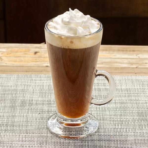 Tall glass of dark coffee topped with a generous swirl of white whipped cream.