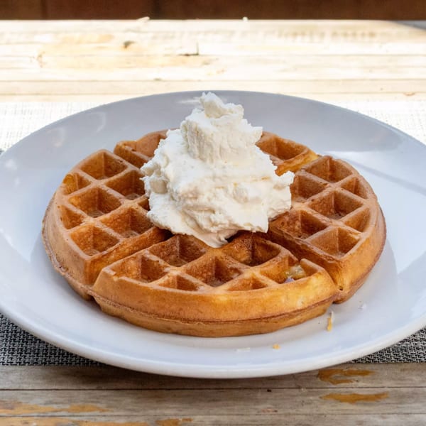 Golden waffle topped with a generous dollop of white whipped cream on a white plate.