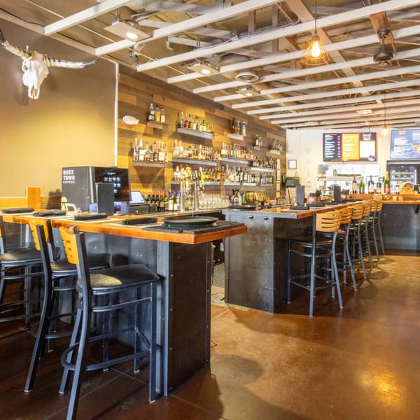 Modern bar interior with high-top tables, bar stools, a fully stocked bar, and a bull skull decoration.