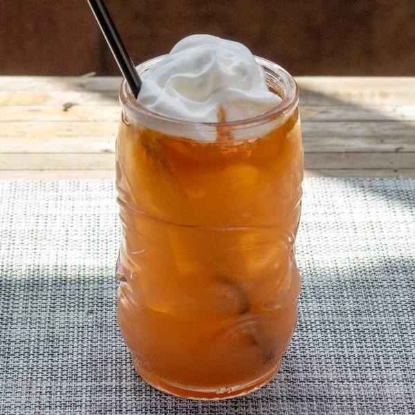 A tiki glass filled with an amber drink, topped with whipped cream and a black straw.