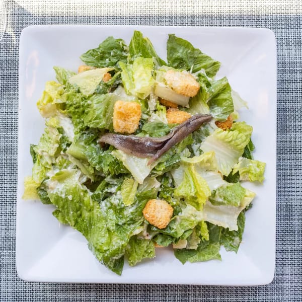 Caesar salad with romaine lettuce, croutons, parmesan cheese, and anchovies on a white plate.