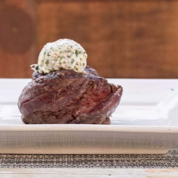 A perfectly cooked steak with a dollop of herb butter on a white rectangular plate.