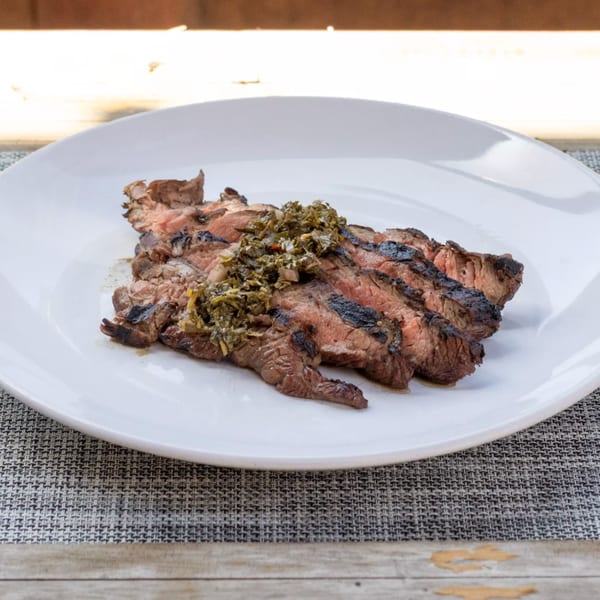 Grilled steak slices topped with green chimichurri sauce on a white plate.