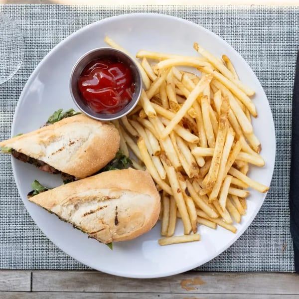 A white plate with a sandwich cut in half, a side of french fries, and a small cup of ketchup.
