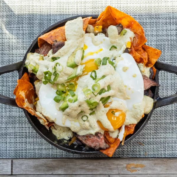 Skillet of steak nachos with fried eggs, creamy sauce, and green onions on a placemat.