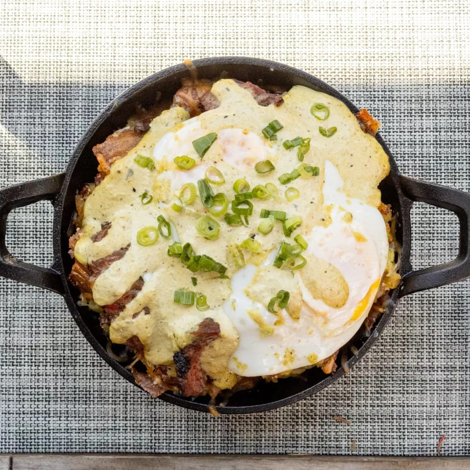 Top-down view of a cast iron skillet with a breakfast dish topped with fried eggs and green onions.